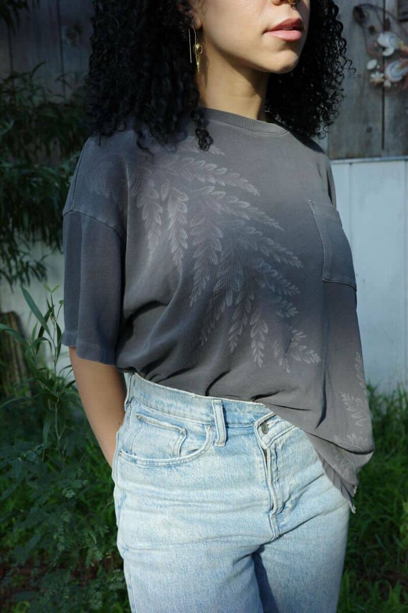 Woman in gray t-shirt with leaf print, standing outdoors.