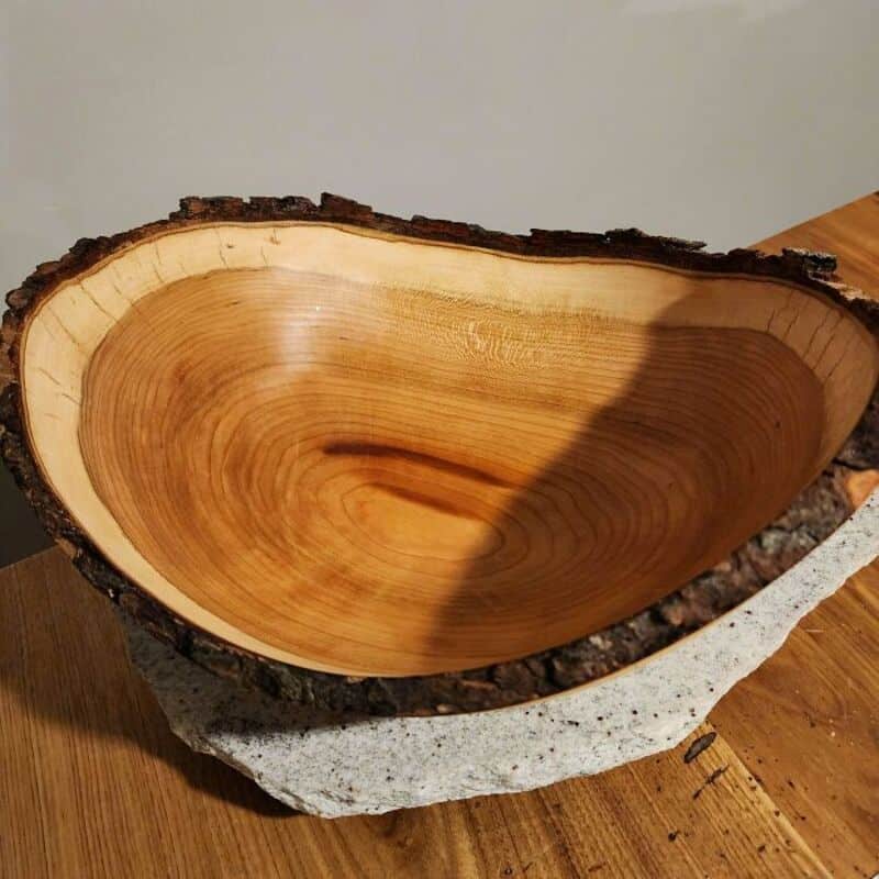Wooden bowl carved from a tree trunk with bark edge, on a wooden surface.