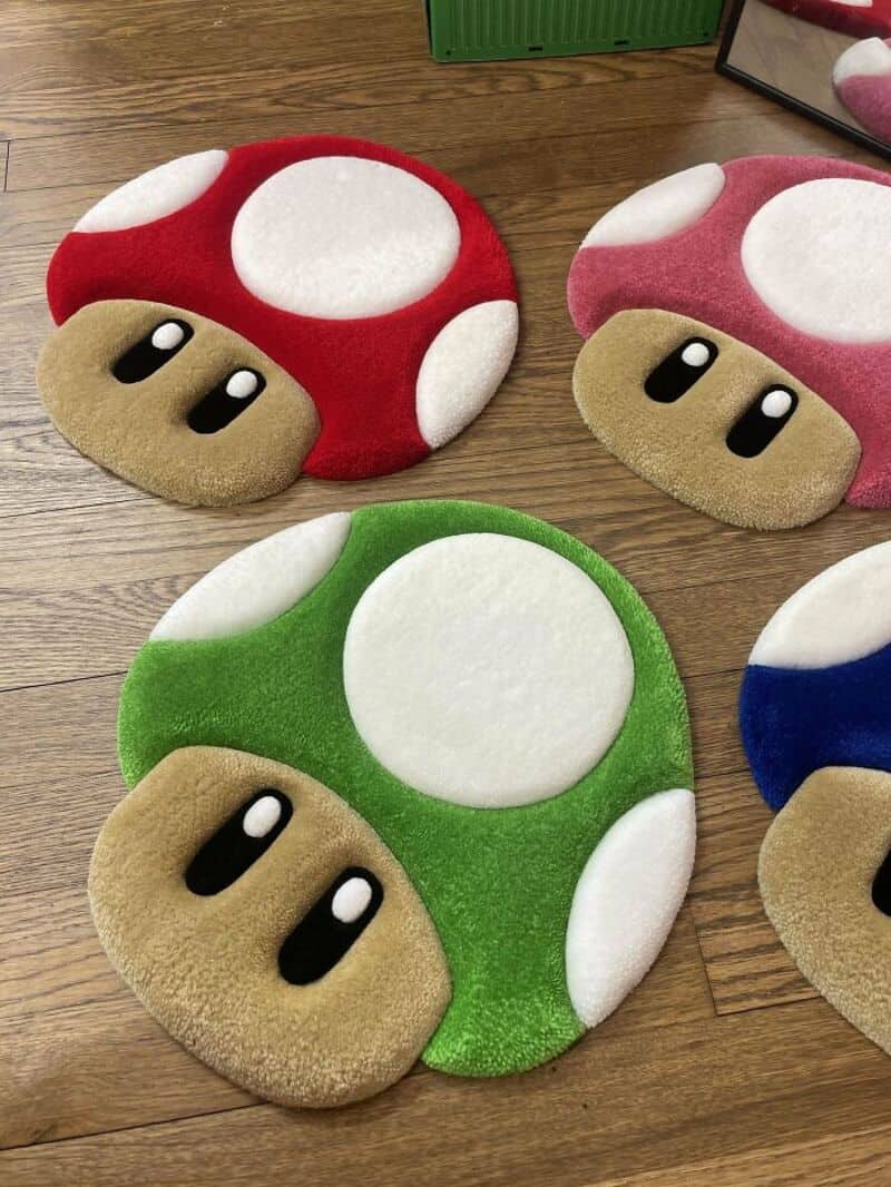 Red and white mushroom plush slippers with beige feet and black eyes, placed on a wooden surface.