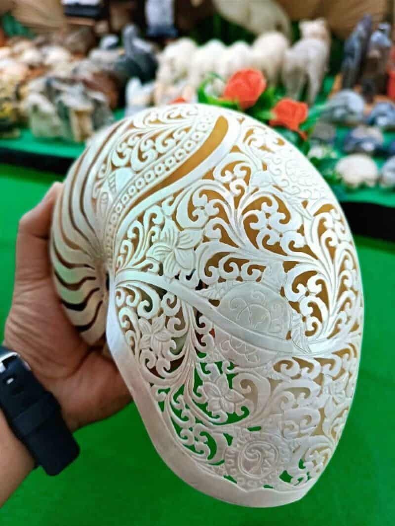 Intricately carved white egg with swirling patterns, held in hand against a background of various ob.