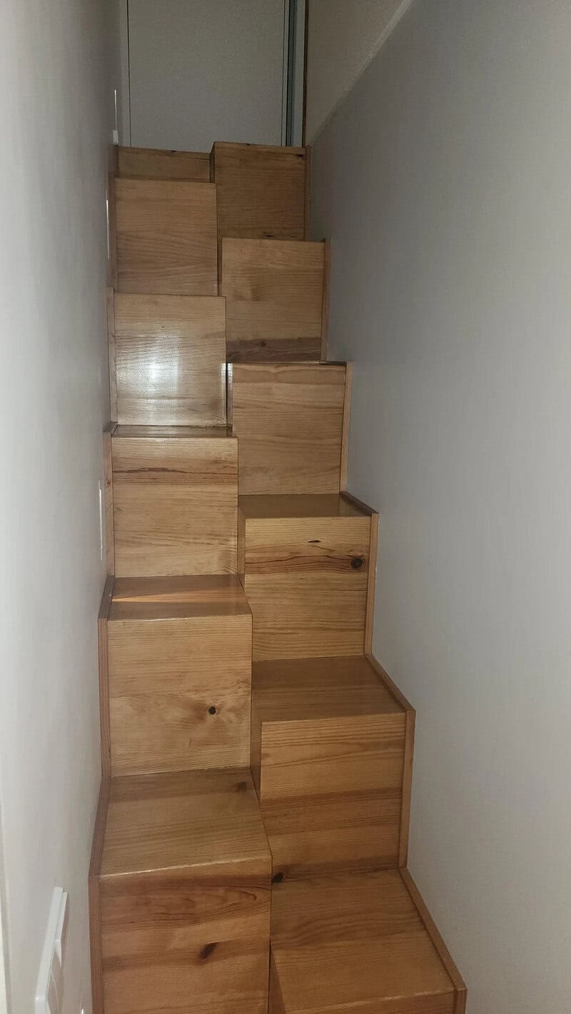 Unique wooden staircase with steps of varying sizes and shapes in a narrow space.