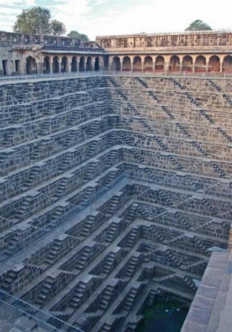 Ancient stepwell with intricate stairs and surrounding arches under a clear sky.