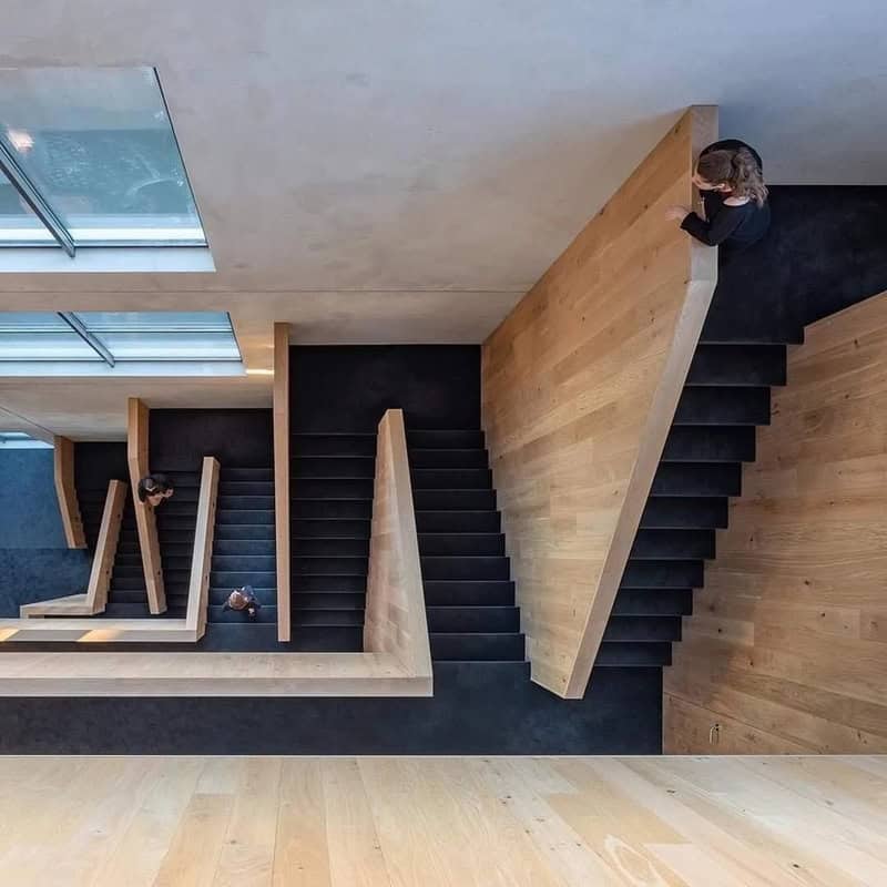 Overhead view of a modern staircase with black steps and wooden sides, with people walking on it.