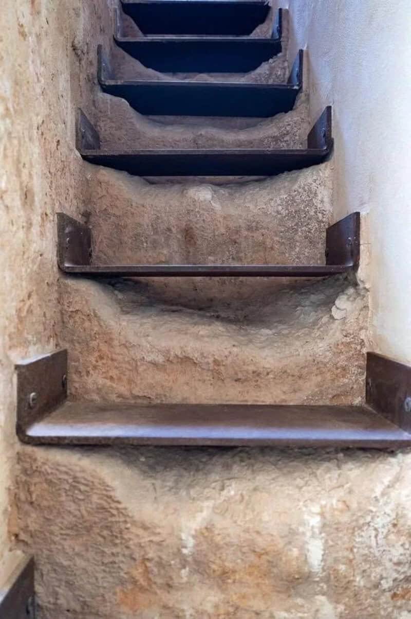 Unusual staircase with uneven steps and metal supports in a narrow space.