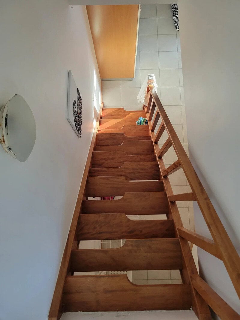 View of a steep wooden staircase from above, leading down to a tiled floor.