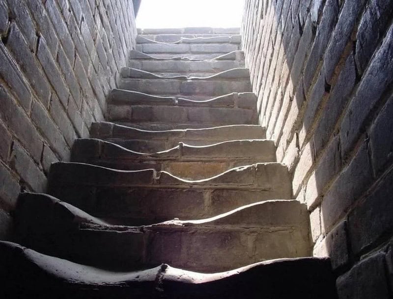 Looking up a steep, narrow staircase with uneven, worn steps between brick walls.