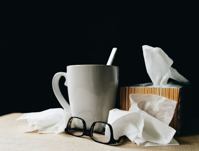 Coffee mug, tissues, glasses, and crumpled tissues on a table.