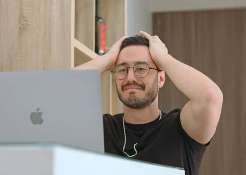 Man with glasses and beard looks frustrated at his computer.