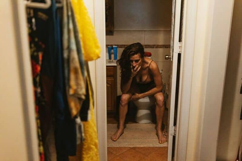 Person sitting on toilet with disheveled hair and distressed expression.