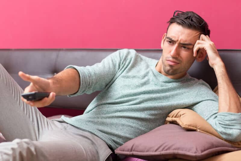 Man looking confused while holding a remote control on a pink background.