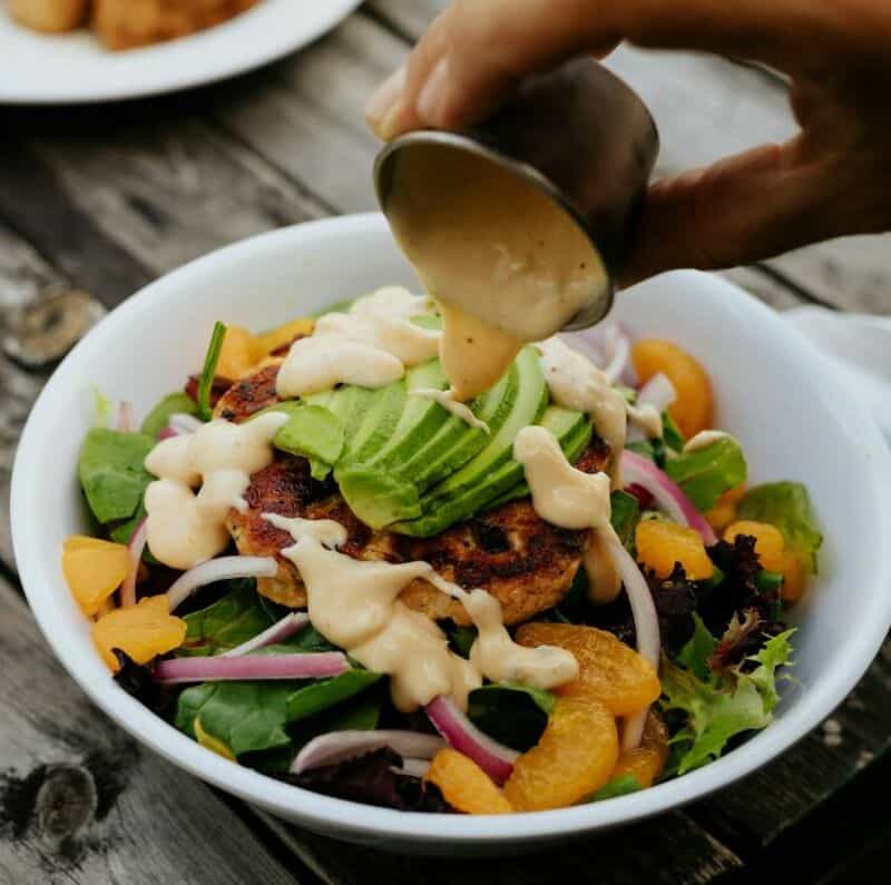 Salad with grilled chicken, avocado, and dressing being poured on top.