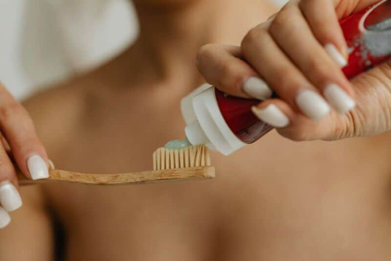 Person applying toothpaste to a toothbrush on bare shoulder.