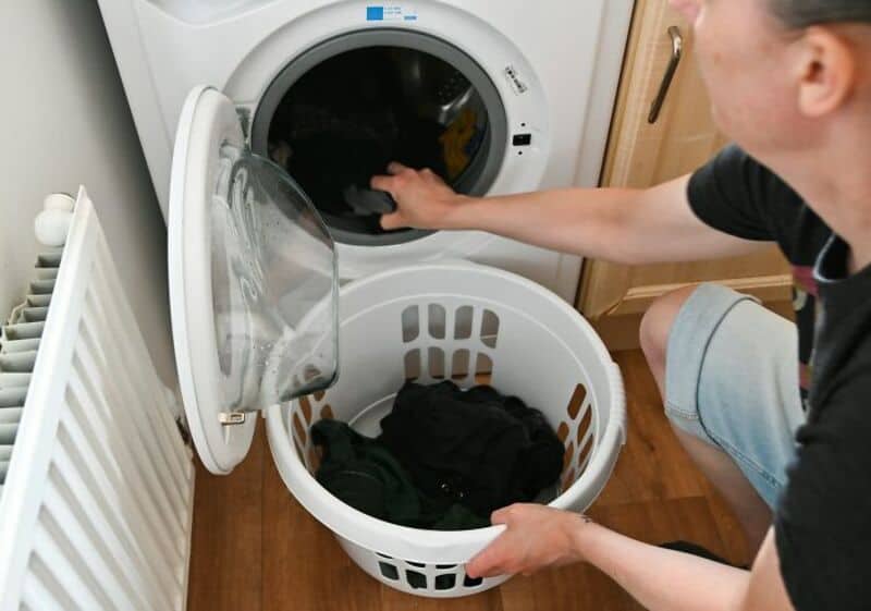 Person putting laundry into washing machine with laundry basket nearby.