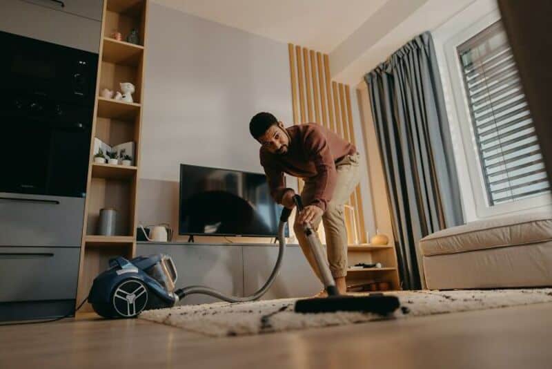 Man vacuuming living room with vacuum cleaner on carpet.
