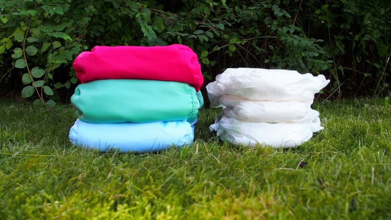 Colorful cloth diapers stacked on grass with greenery background.
