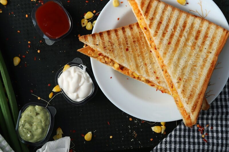 Grilled cheese sandwiches with ketchup, mayonnaise, and guacamole on a black background.