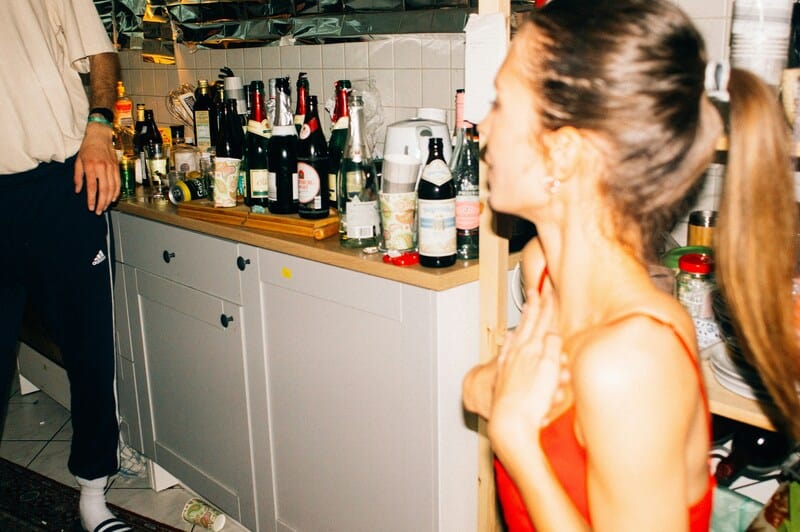 A woman in a red dress standing near a bar with various bottles and glasses.