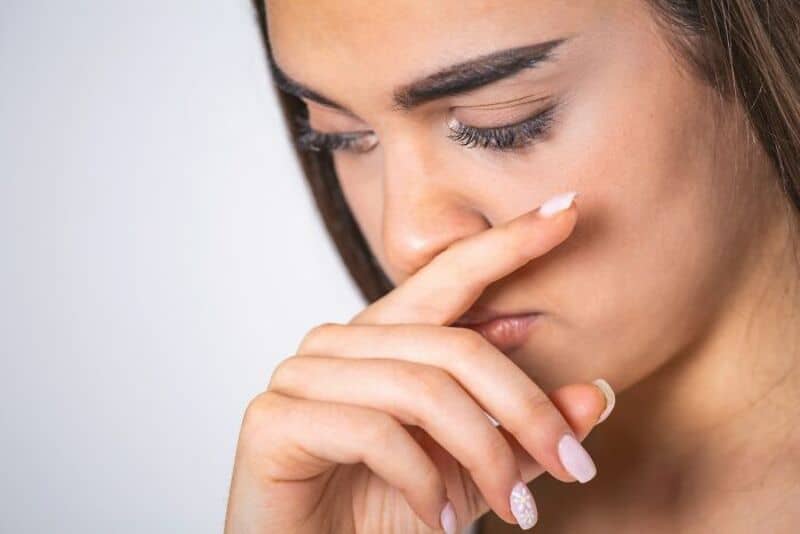Close-up of a woman with her hand over her nose, looking down.
