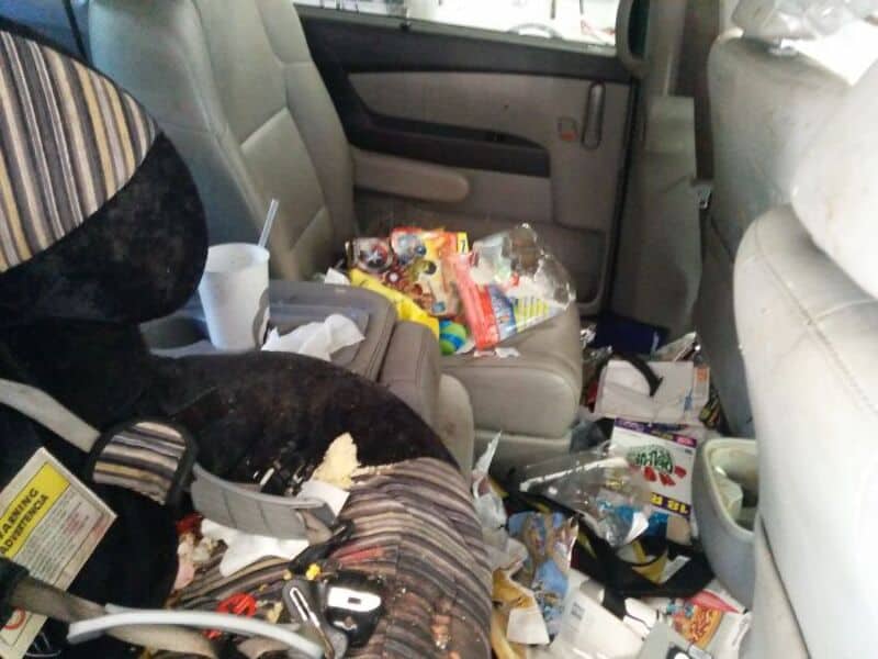 Cluttered car interior with trash and snacks scattered on seats and floor.