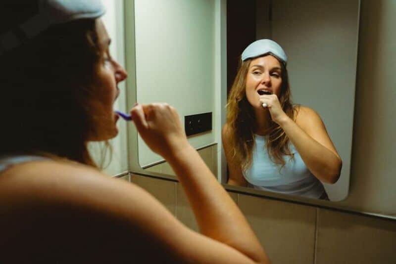 Woman brushing her teeth while looking at herself in the mirror.