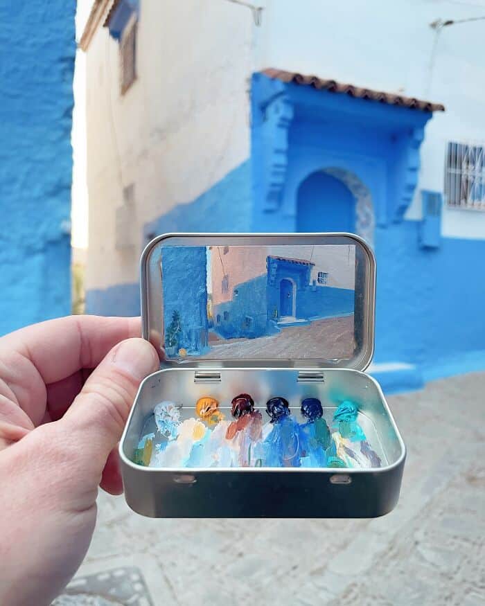 Colorful glass bottles inside a small metal case with a mirror reflecting a blue building facade.