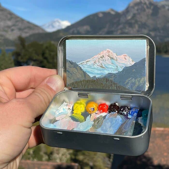 Miniature painting kit with mountain landscape on lid, outdoors scene in background.