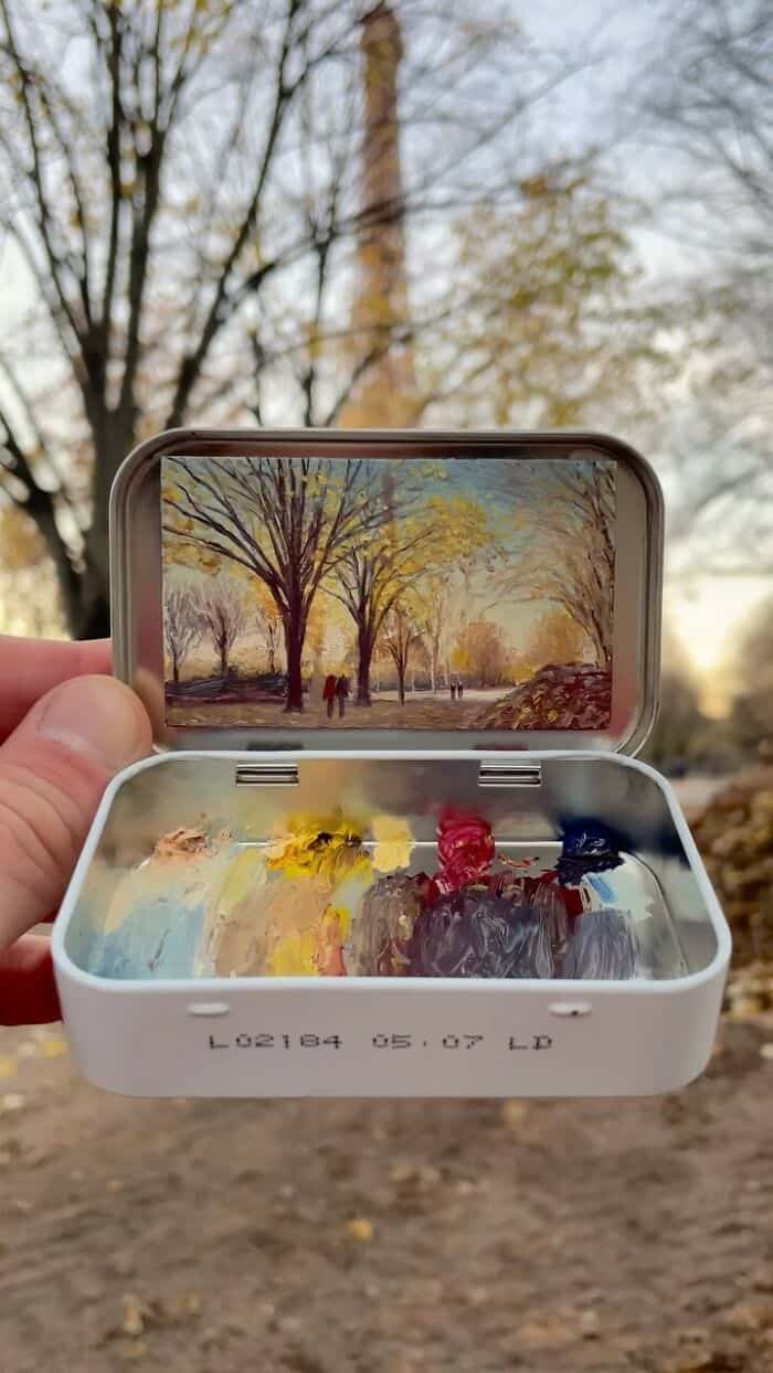 A colorful miniature painting inside a small box with a mirror showing a landscape scene with trees.