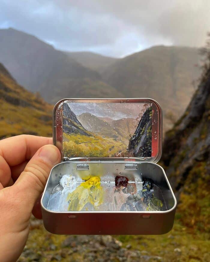 A lush green valley with mountains in the background, viewed through a small mirror held in a person.