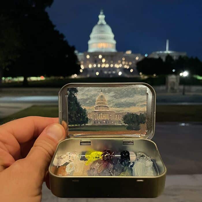 Hand holding a small box with a miniature Capitol building inside, with the real Capitol in the back.