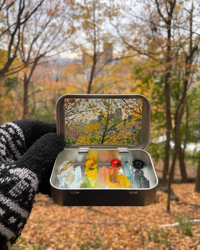 Hand holding a small box with colorful paint tubes outdoors in autumn.