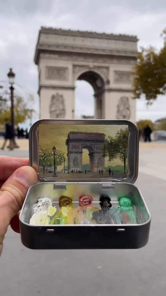 A person holding a small case with colorful candies in front of the Arc de Triomphe in Paris.