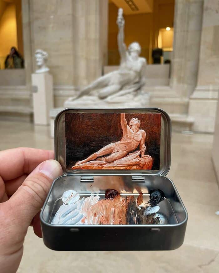 Hand holding a small case with a miniature sculpture and a photo of a classical statue inside.