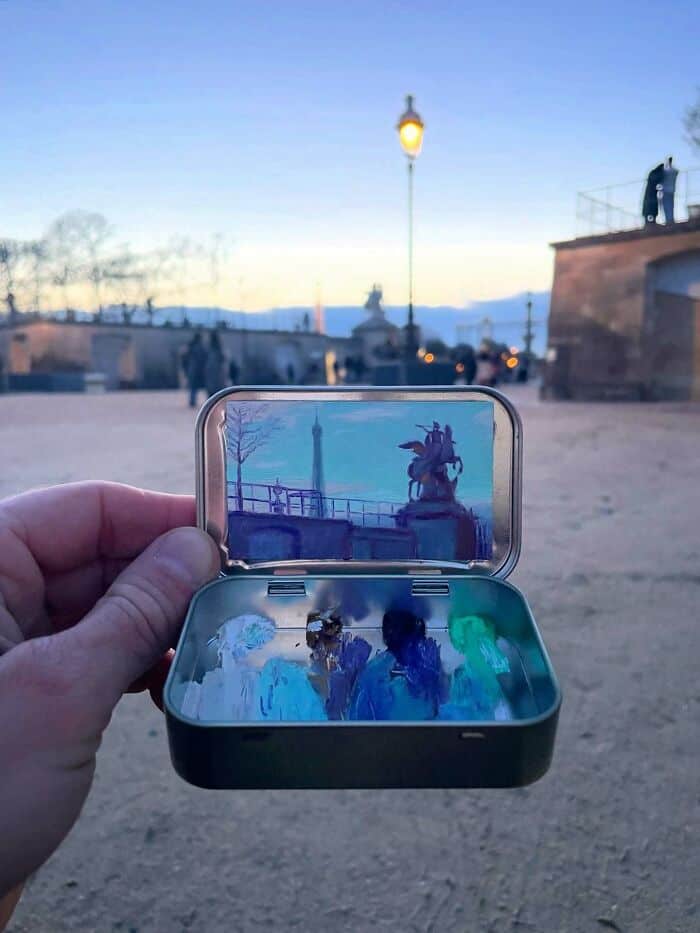 Hand holding a small case with a mirror reflecting a cityscape at dusk.