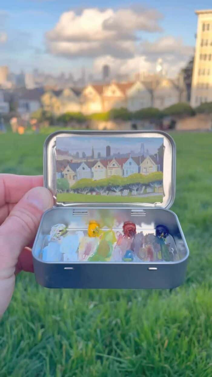 Small metal case with colorful toy figures on ice, cityscape reflection in the mirror.