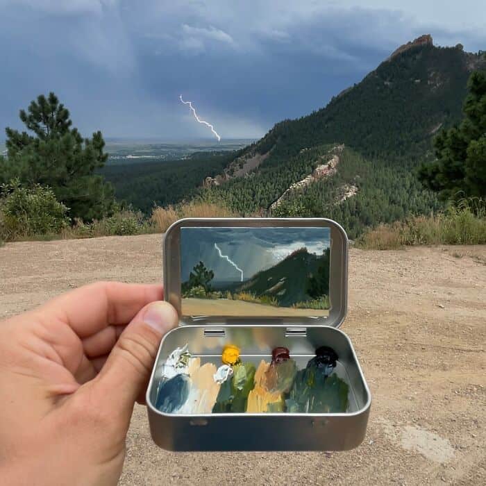 Lightning storm over mountains, reflected in a small mirror held by a hand outdoors.