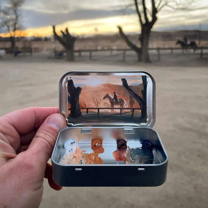 Miniature horse figurines inside a metal case with a sunset scene in the background.