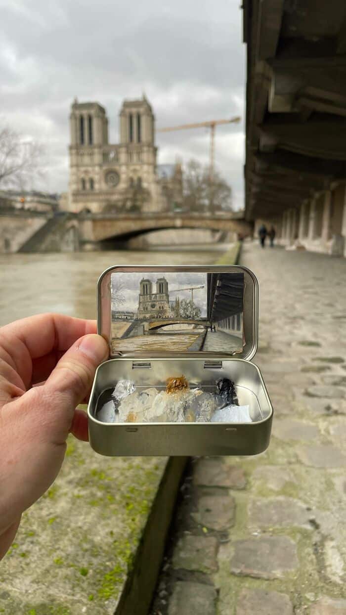 Hand holding a small metal box with a miniature view of Notre Dame in Paris.