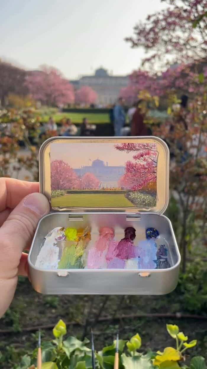 Colorful ice cubes in a small container with a scenic park and pink cherry blossoms in the backgroun.