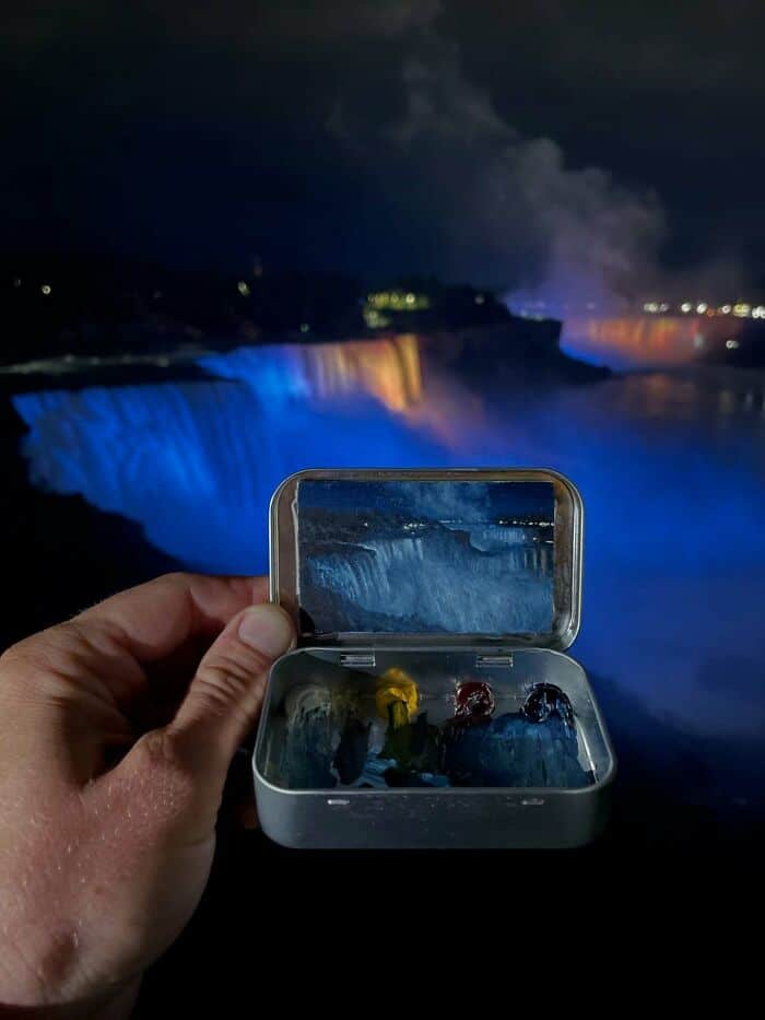 A breathtaking view of Niagara Falls illuminated at night, with a hand holding a waterproof case con.