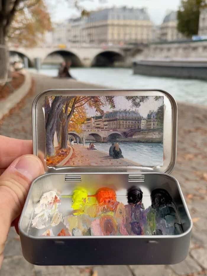 Small paint set with colorful paints and a scenic river view in the background.