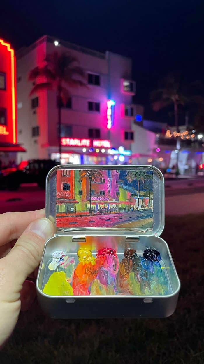 Colorful painted figurines in a clear plastic case at night with neon-lit buildings in the backgroun.