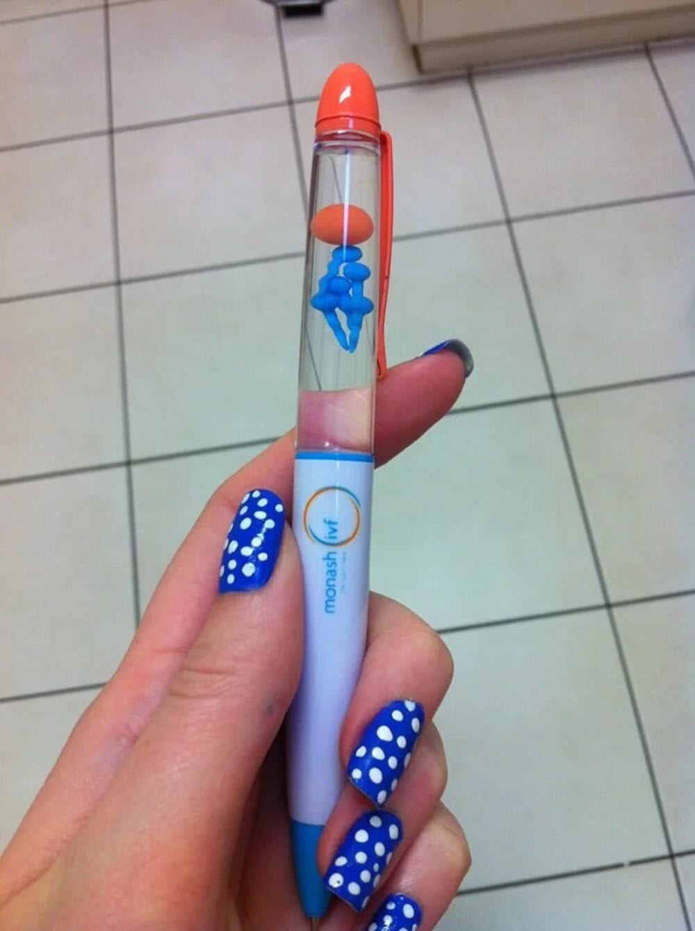 Blue and orange pen with a floating blue figure inside, held by a hand with polka dot nails.
