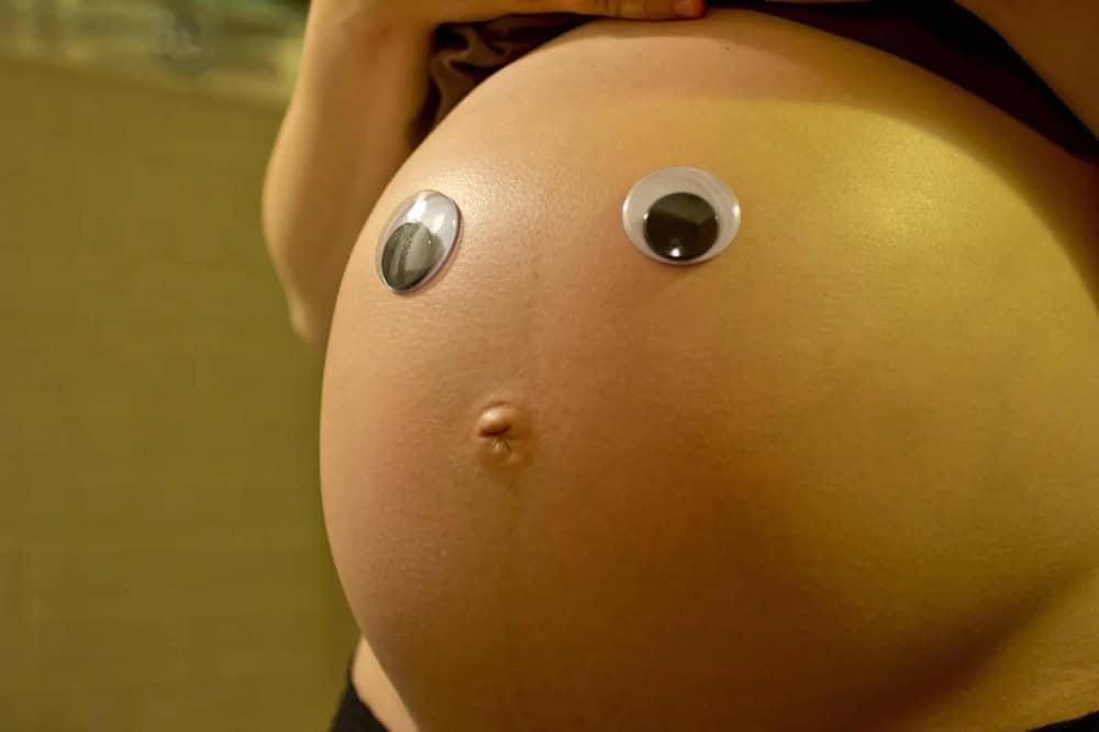 Pregnant belly with googly eyes attached, humorous pregnancy photo.