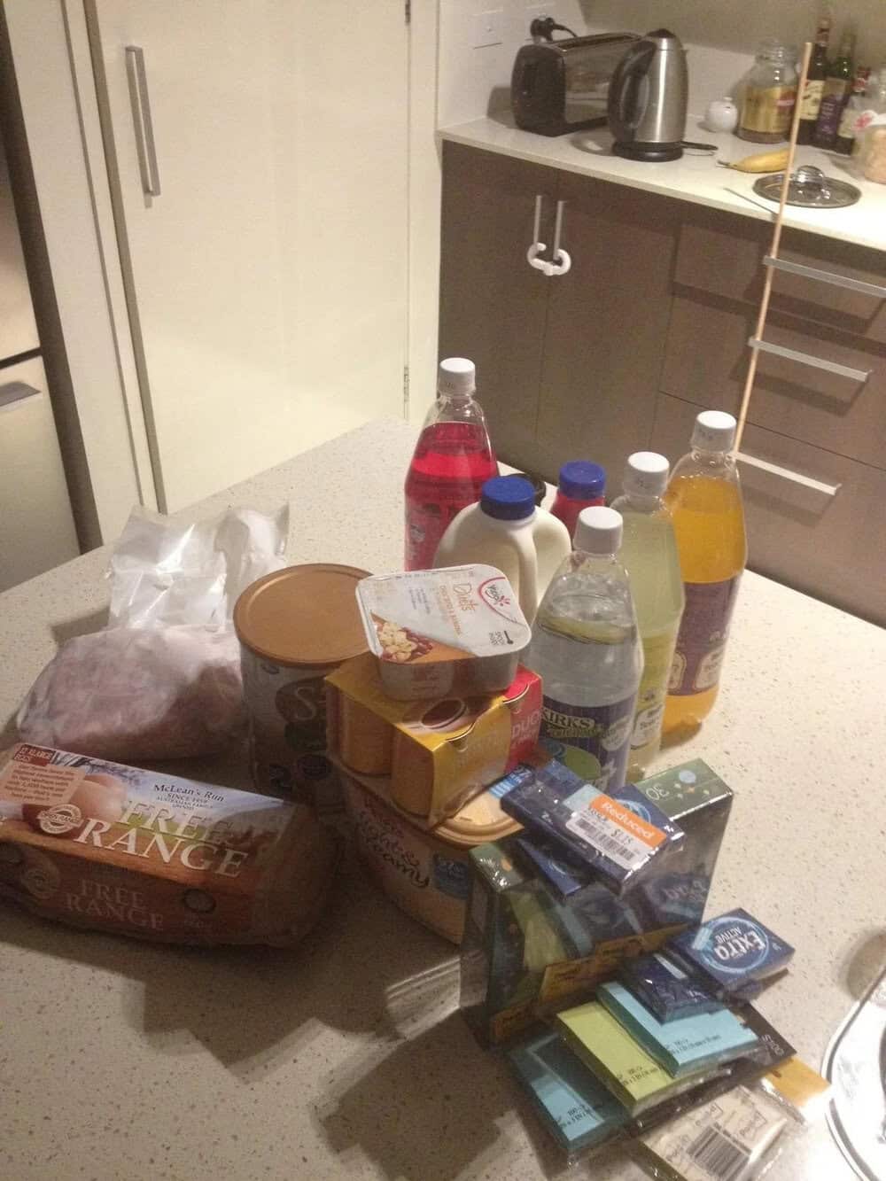 Assorted beverages and snacks on kitchen counter with bottles, boxes, and packaging.