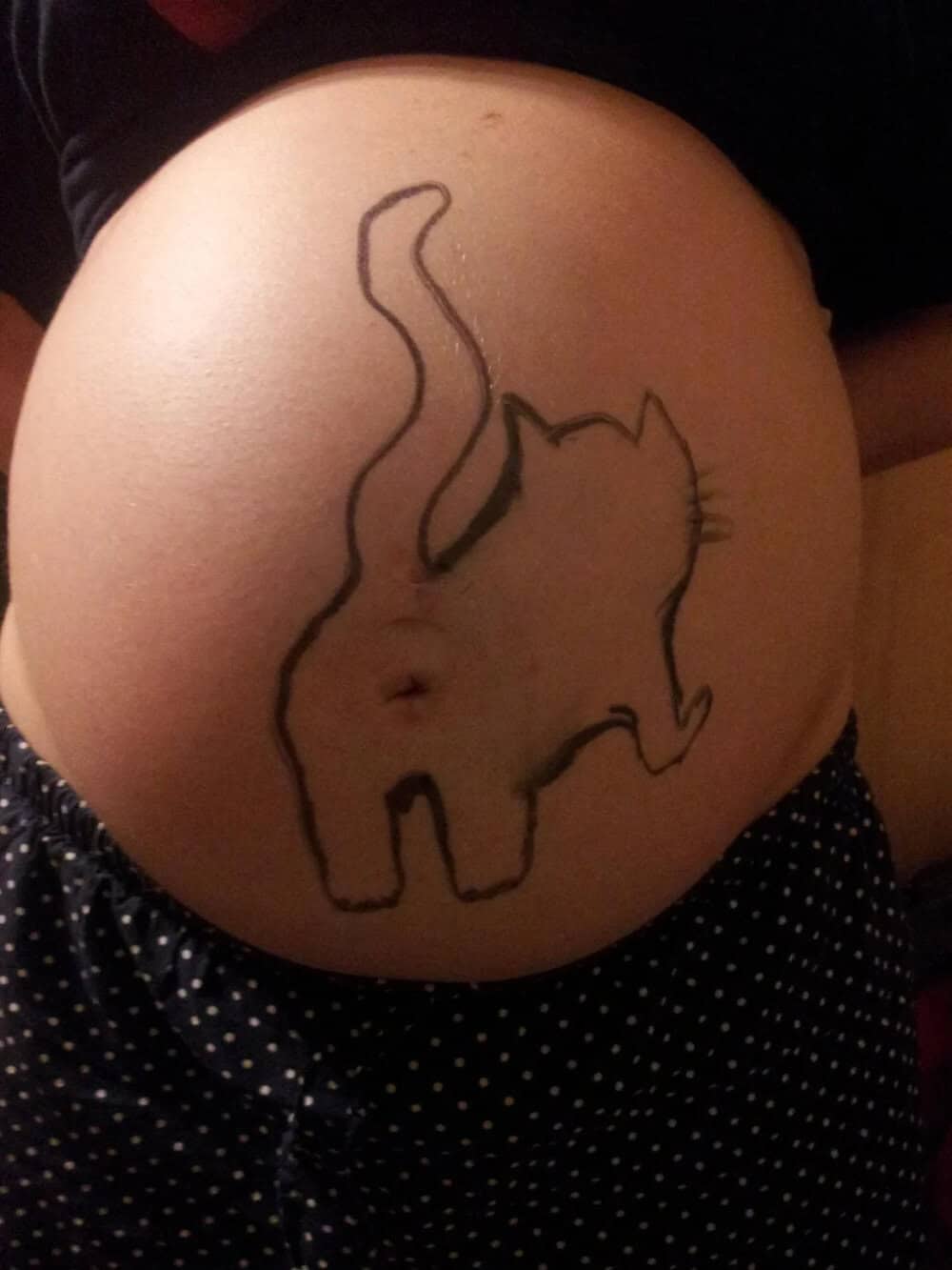 A woman’s belly with a tattoo of a cat outline, including a tail and whiskers.