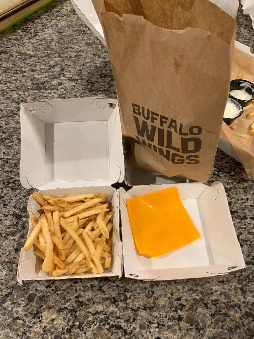 Buffalo Wild Wings takeout meal with fries, cheese, and a paper bag on a granite countertop.