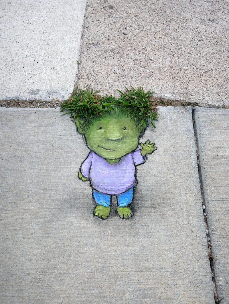 Cute green creature with grass hair waving on sidewalk.