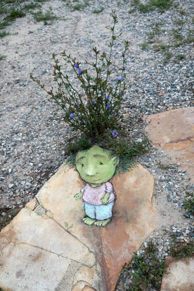 A whimsical garden decoration of a small, painted figure with a plant growing from its head.