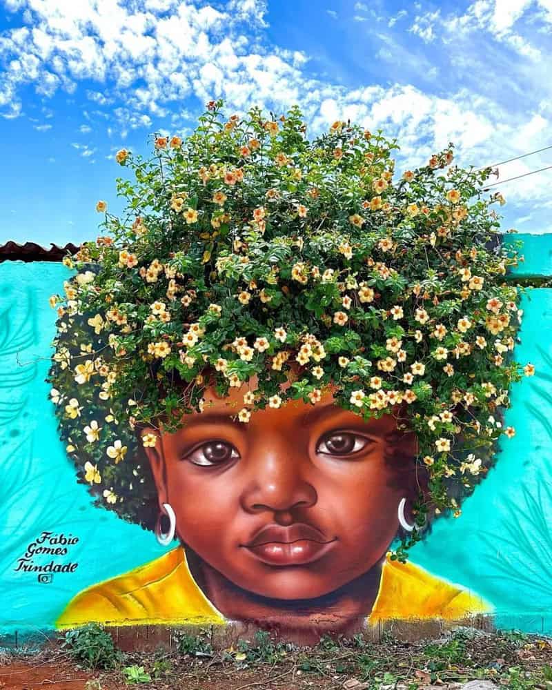 Vibrant mural of a young girl with a large flower crown on her head, bright blue sky background.