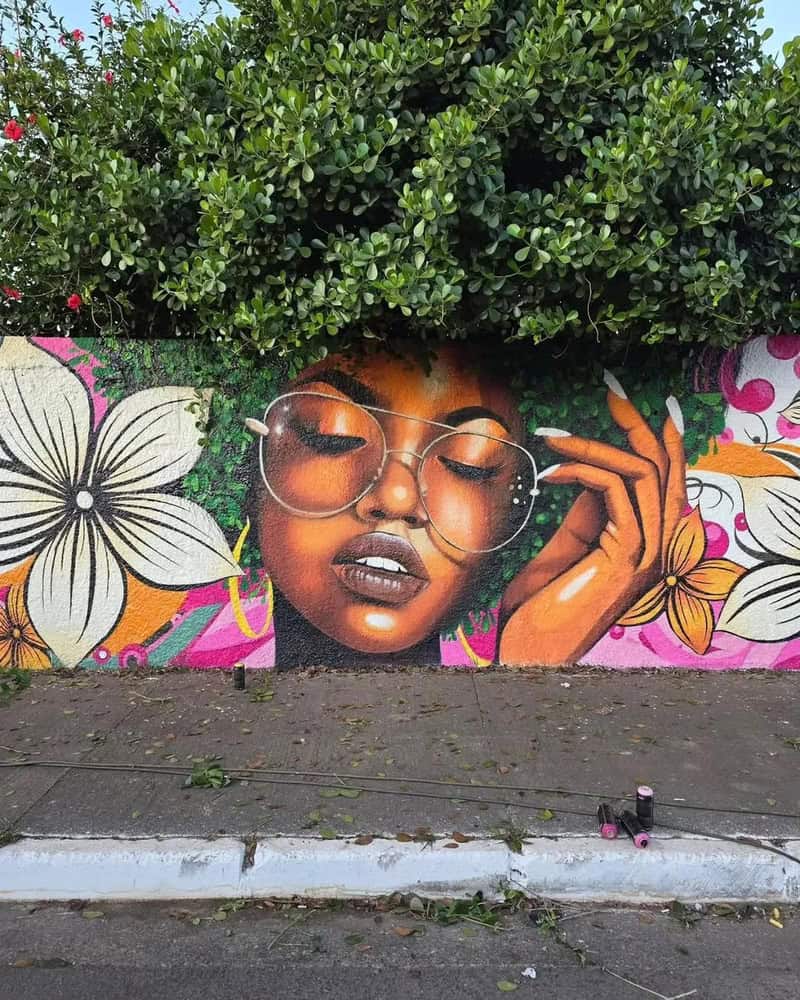 Vibrant mural of a woman with glasses and closed eyes, surrounded by flowers and greenery.